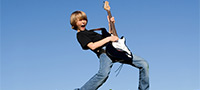 ©iStock.com/mandygodbehear Symbolfoto: Junge mit E-Gitarre in der Hand auf einer Wiese