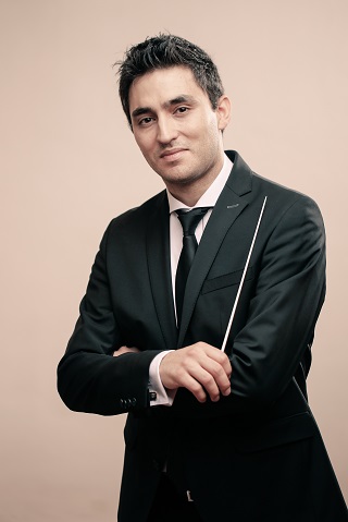 Portraitfoto von einem Mann in Anzug und Krawatte mit einem Dirigierstab in der Hand.