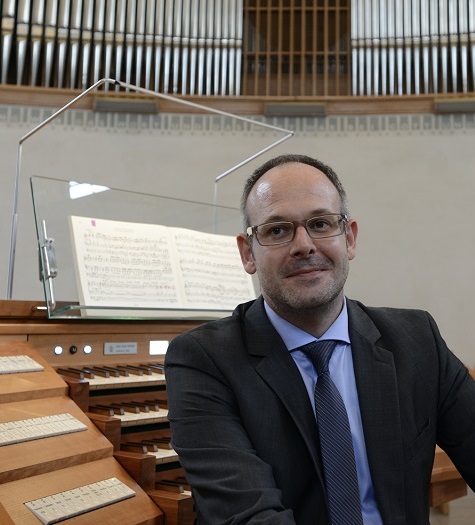 Jürgen Natter Portraitfoto von einem Mann in Anzug und Krawatte sitzend vor einer Orgel